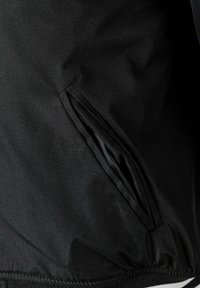 Veste noire avec une texture lisse, dotée d'une poche latérale avec une ouverture discrète et d'un ourlet côtelé. Design minimaliste.