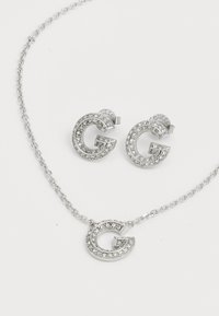 Zilveren sieradenset met een hangerketting en bijpassende stud oorbellen, elke versierd met een kristal-bedekte 'G' ontwerp.