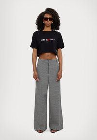 Czarny skrócony t-shirt z białym i czerwonym napisem, w połączeniu z wysokim stanem szerokimi spodniami w czarno-białą kratkę.