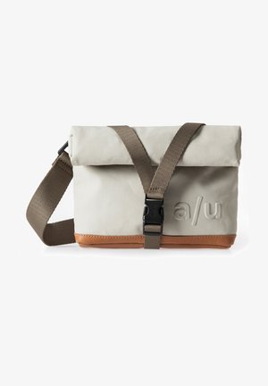 Gefaltete graue Tasche mit braunem Lederboden, verstellbarem Riemen und Kunststoffschnalle. Vorderseite mit geprägtendem Logo. Glatte Stoffstruktur.