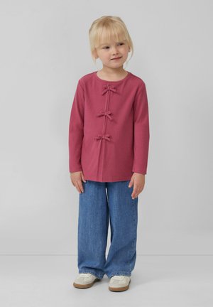 Top rosa a maniche lunghe con costine e tre decorazioni a fiocco, abbinato a jeans blu a gamba larga e scarpe chiare. Design semplice e casual.