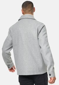 Veste en mélange de laine grise avec un large col, des manches longues et des accents de boutons sur les poignets. La vue arrière montre une coupe décontractée et une texture douce.