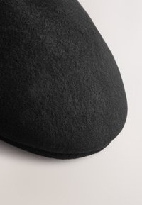 Schwarze Wollfilzmütze mit glatter, abgerundeter Form und einer genähten Kante, die eine weiche Textur aufweist und keine sichtbaren Muster oder Beschläge hat.