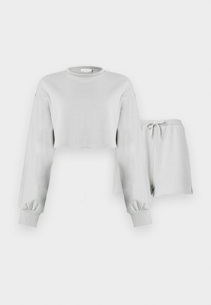 Hellgraues, langärmeliges, croptop Sweatshirt mit gerippten Bündchen, kombiniert mit passenden Shorts mit Kordelzug und Taillenbund vor weißem Hintergrund.