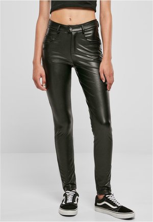 Zwarte, glanzende neplederen broek met een slim fit, hoge taille en achterzakken. Gecombineerd met zwart-witte sneakers.