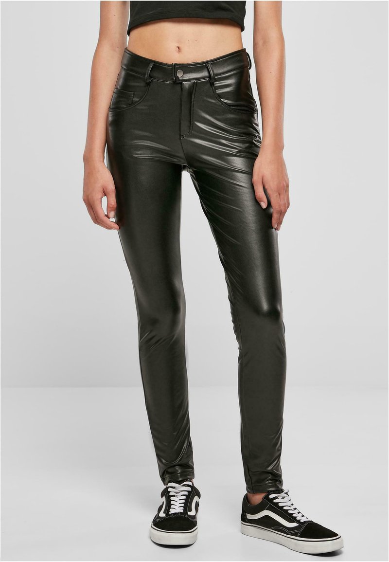 Zwarte, glanzende neplederen broek met een slim fit, hoge taille en achterzakken. Gecombineerd met zwart-witte sneakers.