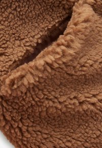 Gros plan d'un tissu marron, doux et duveteux avec une ouverture de poche visible doublée d'un matériau lisse.