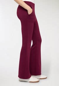 Pantaloni da tuta color bordeaux a zampa, realizzati in materiale morbido; dotati di tasche laterali e ampia fascia in vita, rifiniti con una texture liscia.