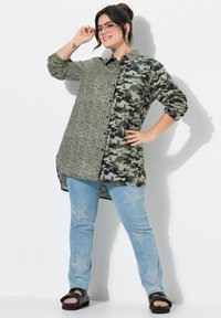Das Langarmhemd hat ein geteiltes Design: Die eine Seite ist mit Leopardenmuster und die andere Seite mit Tarnmuster. Kombiniert mit hellblauen Jeans, die mit Sternmustern versehen sind.