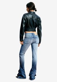 Chaqueta negra de cuero recortada con una textura suave combinada con jeans acampanados azul claro que presentan un desvanecimiento gradual y bolsillos traseros visibles.