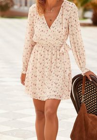 Kukkakuosiin oleva pitkähihaisella mekolla, jossa on beige tausta, vaaleanpunaisia ja purppuranvärisiä kukkia, sekä sidottu vyötärö. Korostettu röyhelöhelmaan.