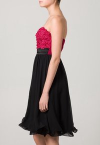 Axelös klänning med en rosa blommig överdel och svart kjol. Tillverkad av mjukt tyg med volangkant och figurnära midja.