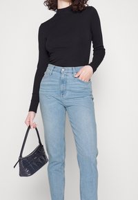 Svart ribbad långärmad topp som är ihopkopplad med högmidjade ljusblå denimjeans. Håller en liten svart kviltad handväska.