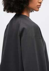 Σκούρο γκρι φούτερ με άνετη εφαρμογή, στρογγυλή λαιμόκοψη και λεία υφή. Σημαντικά χαρακτηριστικά περιλαμβάνουν μια διακριτική ραφή στον ώμο.