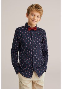 Mörkblå skjorta med knappar och mönster av röda polkagrisar, kombinerad med en röd fluga. Har lång ärm och krage.