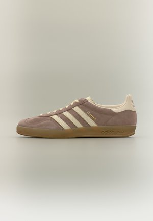 Sneaker Adidas Gazelle en daim mauve douce avec des bandes crème et une semelle en gomme, vue de côté sur fond neutre.