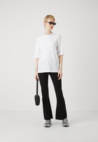 Tricou alb supradimensionat, pantaloni negri evazați și adidași gri. Accesoriu: geantă mică crossbody neagră. Model purtând ochelari de soare negri.