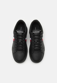 Czarne skórzane sneakersy z okrągłym noskiem, sznurowadłami i charakterystycznym logo Hilfiger. Posiadają czerwone, białe i granatowe paski po bokach.