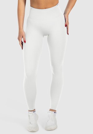 Witte high-waisted leggings van een soepele, rekbare stof. Kenmerkt zich door een geribbelde tailleband en een getailleerd silhouet, gecombineerd met witte sneakers.