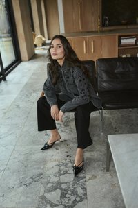 Crna traper košulja s ukrasnom vezom, crne hlače visokog struka i crne mule uskog vrha s detaljem u obliku mašne; moderni unutarnji ambijent.