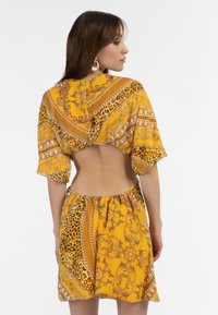 Rochie scurtă galbenă cu imprimeu leopard și modele aurii ornate, cu un design la spate scurt și mâneci scurte.