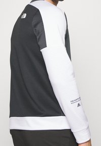 Felpa atletica in bianco e nero con corpo nero testurizzato, maniche bianche a righe e dettagli con logo sulle spalle e sui polsi.