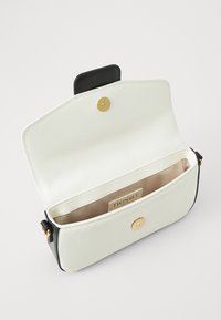Witte leren handtas met zwarte accenten, magnetische drukknoopsluiting, gouden hardware en een gladde binnenvoering met een merklabel.