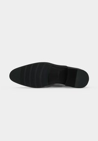 Semelle de chaussure habillée noire avec motifs de grip texturés et petit talon, présentée sur fond blanc.