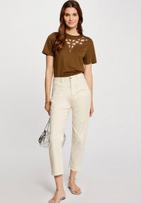 Brązowy t-shirt z krótkim rękawem z koronkowym wzorem; kremowe spodnie prostego kroju; srebrna torebka; sandały na cienkich paskach.