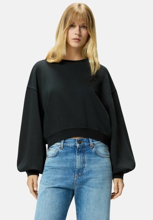 Sudadera negra corta con mangas anchas, con un cuello y un dobladillo acanalados. Combinada con jeans de tiro alto de color azul claro.