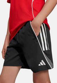 Zwarte sportieve shorts met witte strepen, gemaakt van lichtgewicht stof, met zijzakken en een Adidas-logo op de zoom. Heeft een grijze accent.