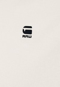 Hvit t-skjorte med en jevn tekstur som har en liten svart "RAW"-logo på venstre side, som fremhever minimalisme.