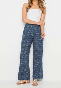 Modré široké kalhoty se vzorem květin. Vyrobeno z měkké tkaniny, mají elastický pas a volný střih, doplněné sandály.