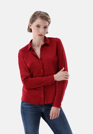 Rotes Hemd mit Kragen und langen Ärmeln, aus glattem Stoff und taillierter Passform, kombiniert mit blauen Jeans.
