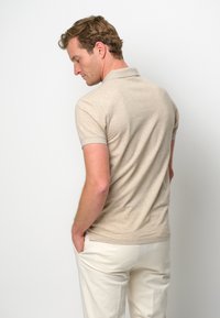 Beige kortärmad polo skjorta med en klassisk krage och ribbade muddar, matchad med ljusa byxor som är stoppade i fickorna.