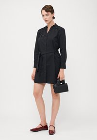 Abito nero a camicia con colletto e chiusura frontale a bottoni, con decorazioni di perline sulle spalle, vita cintrata e un tessuto leggero.