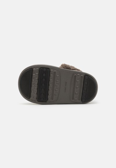 Semelle de pantoufle grise avec une surface texturée, présentant une combinaison de motifs lisses et striés pour une meilleure adhérence et stabilité.