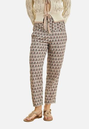 Pantalones beige con estampado hasta el tobillo combinados con un cárdigan de punto crema y sandalias tipo chancla marrones en una persona de pie.