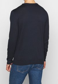 Mörkblå långärmad tröja med rund halsringning, stickad textur, ribbade ärmslut och nederkant, som kombineras med blå denimjeans.