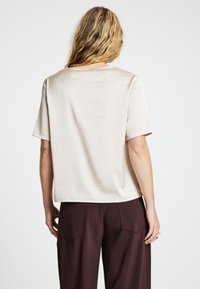 Top beige in satin con maniche corte, vestibilità rilassata e texture liscia. Abbinato a pantaloni marroni a gamba larga con tasche posteriori.