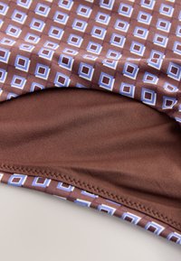 Gros plan sur un tissu marron avec un motif de carrés bleus et blancs, montrant des coutures détaillées et des bords pliés.