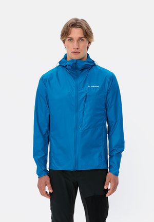 Giacca leggera blu con cappuccio, tasca a zip sul petto, polsini elasticizzati e una texture liscia. Presenta il logo sul lato sinistro superiore.