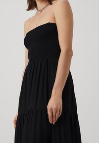 Robe noire sans bretelles avec un corsage smocké et une jupe fluide. Le tissu est léger, avec une texture lisse et un design à volants.