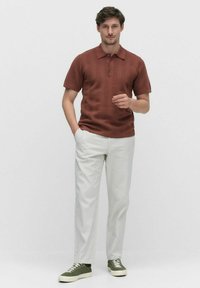 Brun, struktureret polo t-shirt med korte ærmer og krave, parret med lysegrå bukser og grønne sneakers.