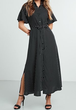 Black polka dot maxi dress with short sleeves, button-down front, and a tie belt at the waist. Features side slits for ease of movement.
