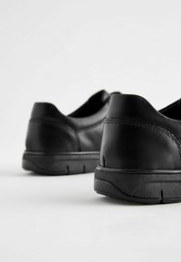 Chaussures en cuir noir avec une texture lisse et un talon arrondi. Semelles en caoutchouc épaisses avec un motif de semelle subtil. Détails de couture minimalistes.