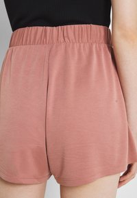 Měkké, růžové šortky s elastickým pasem. Tkanina má hladkou texturu, nabízí volný, pohodlný střih a kulaté zakončení.