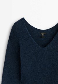 Mørkeblå tekstureret uldsweater med V-hals og synlige tøj-tags på en hvid baggrund.