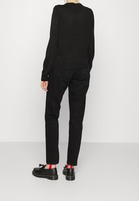 Svart långärmad topp och matchande jeans; svarta skor med tofsdetaljer; röda och svarta randiga strumpor synliga. Övergripande monokromatisk look.