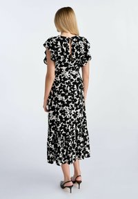 Czarna i biała sukienka w kwiaty z falbaniastymi rękawami, dekoltem w kształcie łezki i rozkloszowanym dołem. Noszona z czarnymi sandałami na obcasie.